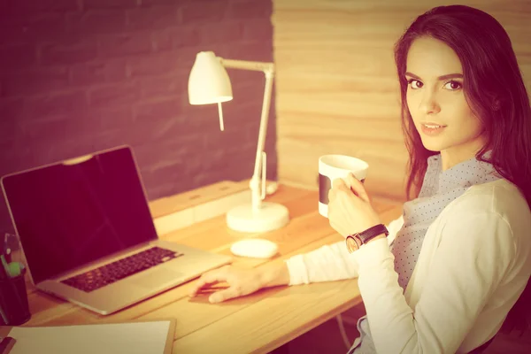 Porträt einer entspannten jungen Frau, die mit einer Tasse Kaffee an ihrem Schreibtisch sitzt — Stockfoto