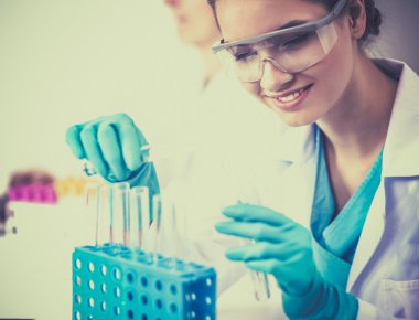 Kadın araştırmacı, beyaz arka planda izole edilmiş ilaç şişeleri ve mataralarla çevrili.