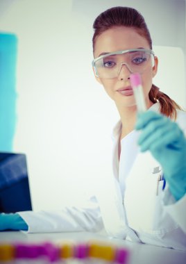 Kadın araştırmacı, beyaz arka planda izole edilmiş ilaç şişeleri ve mataralarla çevrili.