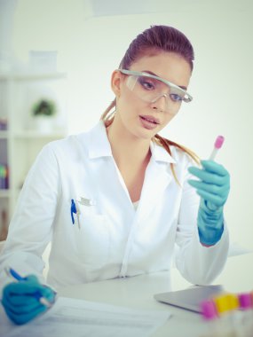 Kadın araştırmacının etrafı ilaç şişeleri ve mataralarla çevrili.