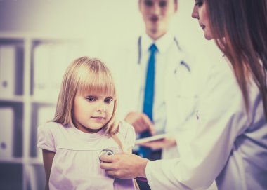 Kadın doktor ameliyatta steteskopla çocuğu muayene ediyor.