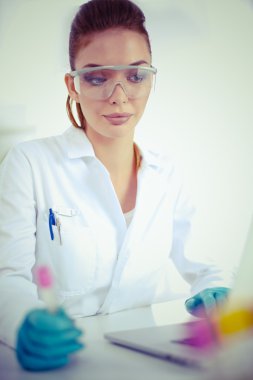 Kadın araştırmacının etrafı ilaç şişeleri ve mataralarla çevrili.