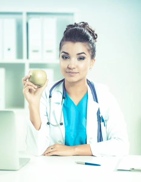 Žena lékař ruka drží zelené jablko, sedí za stolem — Stock fotografie