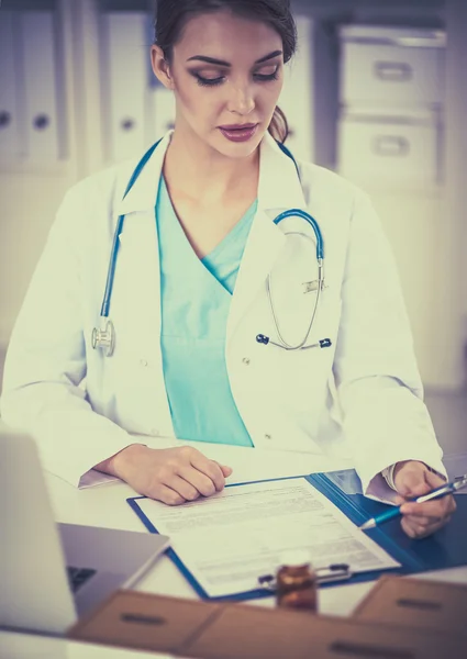 Belle jeune femme médecin souriante assise au bureau et écrivant. — Photo