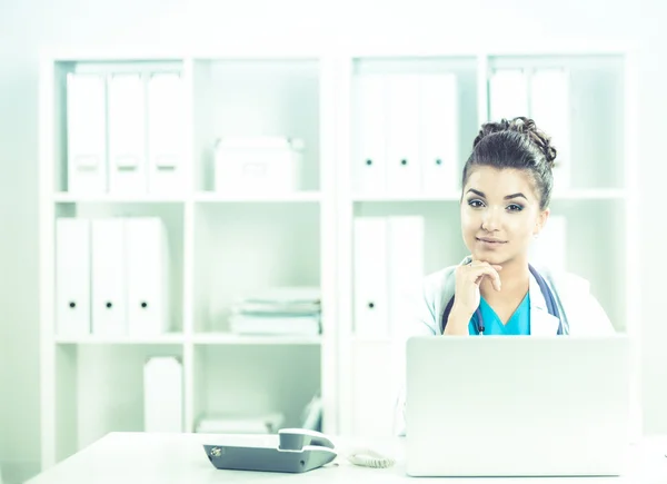 Female doctor sitting on the desk and working a laptop in hospital — Stock Photo, Image