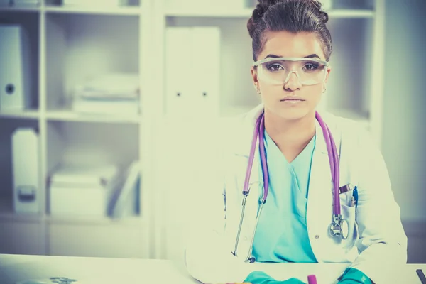 Beautiful young smiling female doctor sitting at the desk and writing. — Stock Photo, Image