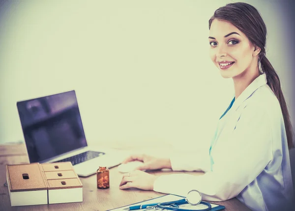 Belle jeune femme médecin souriante assise au bureau et écrivant. — Photo