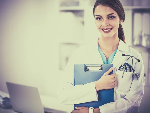 Médico sonriente con una carpeta en uniforme de pie en el hospital —  Fotos de Stock