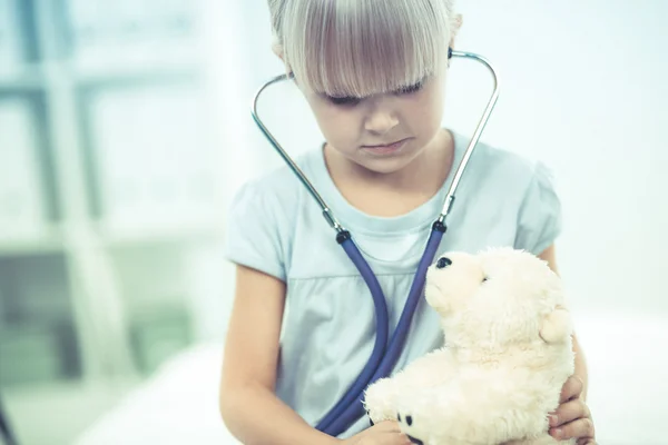 Klein meisje onderzoekt haar teddybeer met stethoscoop. — Stockfoto