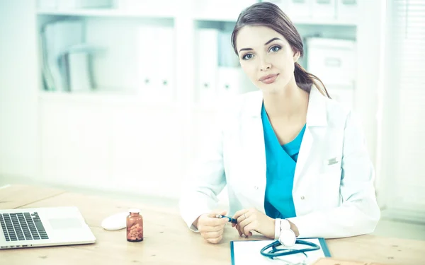 Belle jeune femme médecin souriante assise au bureau et écrivant. — Photo