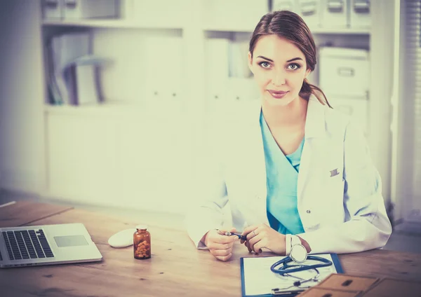 Güzel, genç, gülümseyen bayan doktor masada oturuyor ve yazıyor.. — Stok fotoğraf