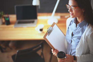 Masanın yanında dizüstü bilgisayarı ve bir fincan kahveyle duran genç bir kadın.