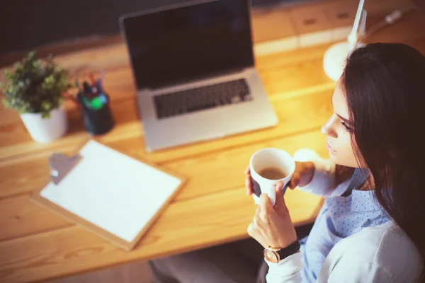Porträt einer entspannten jungen Frau, die mit einer Tasse Kaffee an ihrem Schreibtisch sitzt — Stockfoto