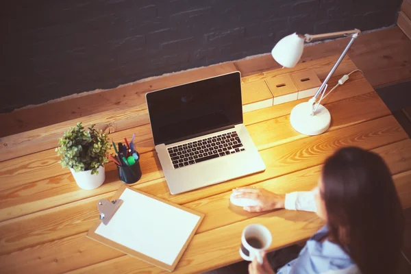 Portret van een ontspannen jonge vrouw aan haar bureau met een kop koffie — Stockfoto