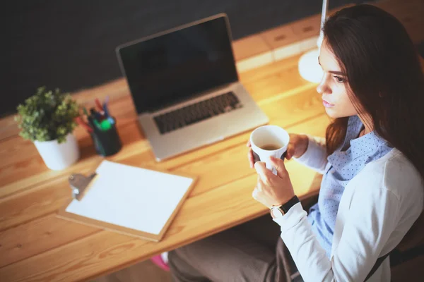 Porträt einer entspannten jungen Frau, die mit einer Tasse Kaffee an ihrem Schreibtisch sitzt — Stockfoto