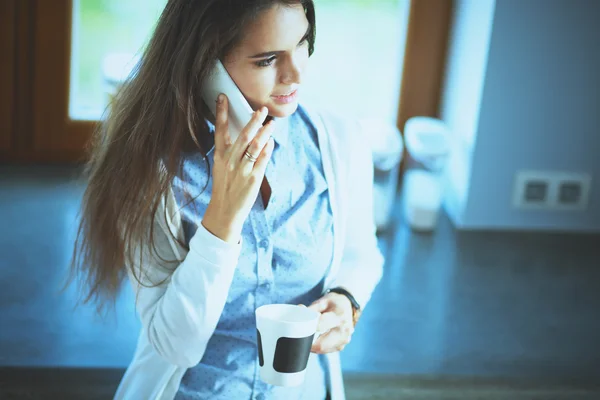 Szczęśliwa kobieta pije herbatę w kuchni w domu i rozmawia przez telefon — Zdjęcie stockowe