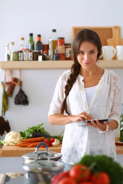Mutfakta yemek yapmak için tablet bilgisayar kullanan genç bir kadın. .