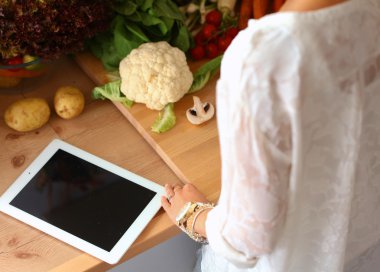 Mutfakta yemek yapmak için tablet bilgisayar kullanan genç bir kadın. .