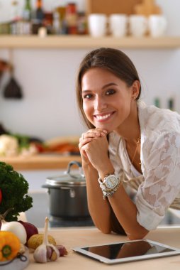 Mutfakta yemek yapmak için tablet bilgisayar kullanan genç bir kadın. .