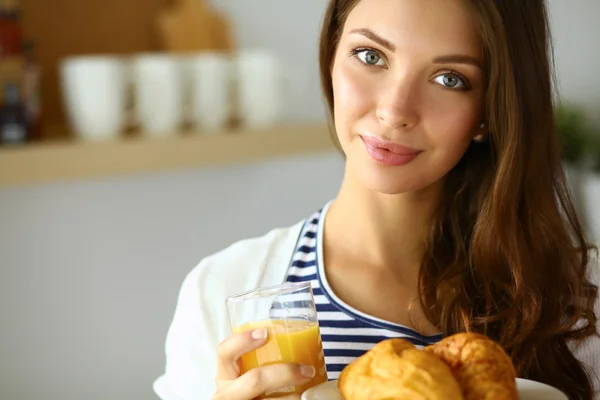 Mujer joven con vaso de jugo y pasteles de pie en la cocina . —  Fotos de Stock