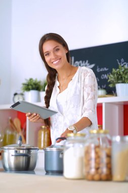 Mutfakta yemek yapmak için tablet bilgisayar kullanan genç bir kadın.