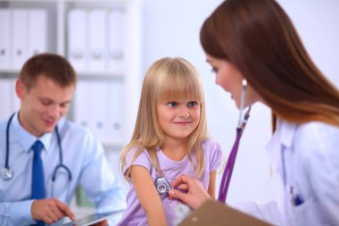 Kadın doktor ameliyatta steteskopla çocuğu muayene ediyor.