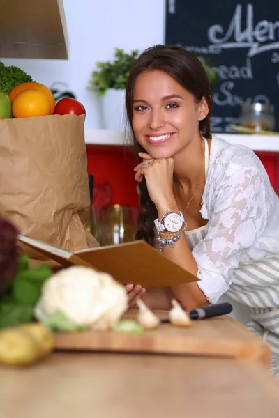 Young woman reading cookbook in the kitchen, looking for recipe