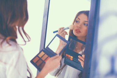 Genç ve güzel bir kadın aynanın yanında makyaj yapıyor.