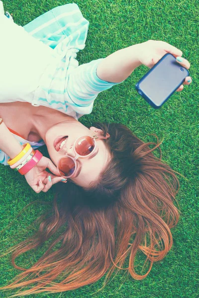 Bela jovem mulher fazendo selfie por seu telefone enquanto deitado na grama verde — Fotografia de Stock