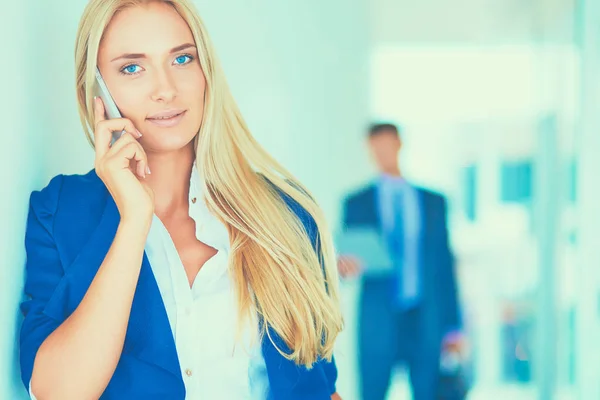 Zakenvrouw staat tegen kantoorraam te praten op mobiele telefoon — Stockfoto