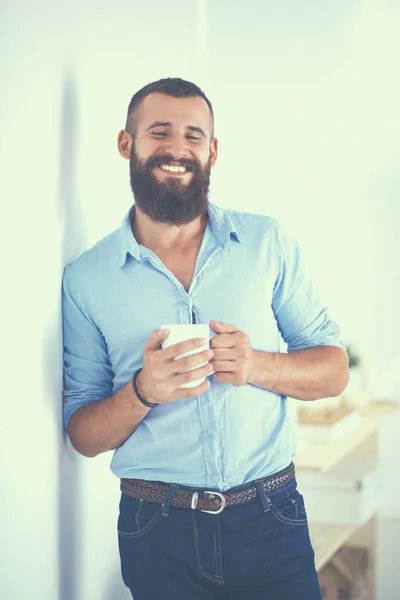 壁の近くに立って、一杯のコーヒーを保持している若い男 — ストック写真