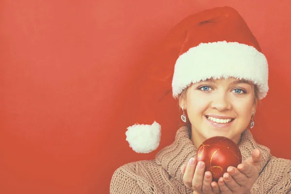 Pretty brunette woman in shirt and santas hat holding red christmas ball — Stock Photo, Image