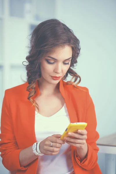 Beautiful businesswoman using cell phone standing in office — Stock Photo, Image