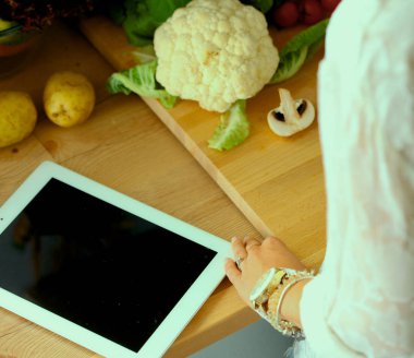 Mutfakta yemek yapmak için tablet bilgisayar kullanan genç bir kadın. .