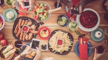 Bir grup insan ahşap masada otururken birlikte yemek yiyorlar.