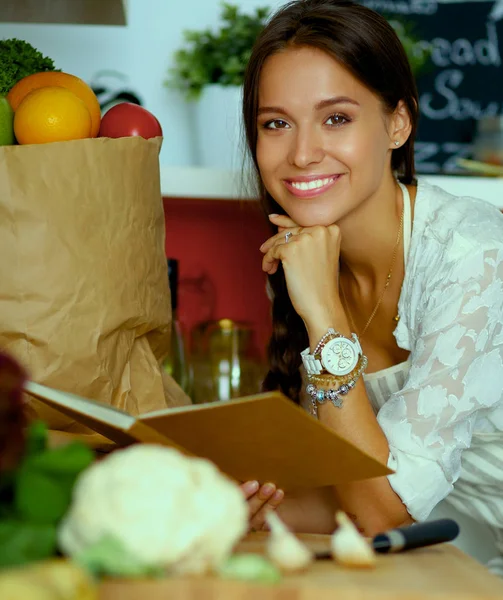 Young woman reading cookbook in the kitchen, looking for recipe