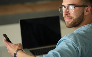 Genç adam kullanarak telefon ve dizüstü bilgisayarda çalışır