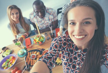 Öğle yemeği sırasında selfie çeken bir grup insan.