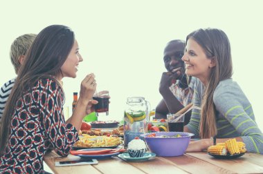 Bir grup insan ahşap masada otururken birlikte yemek yiyorlar.