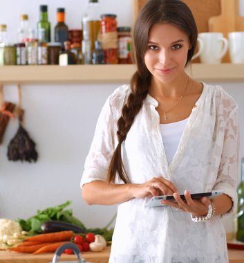 Mutfakta yemek yapmak için tablet bilgisayar kullanan genç bir kadın. .