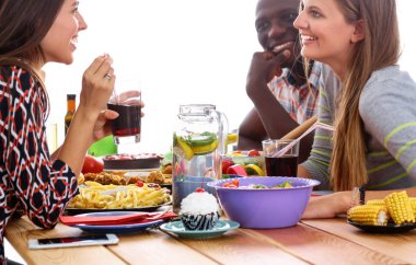 Bir grup insan ahşap masada otururken birlikte yemek yiyorlar.