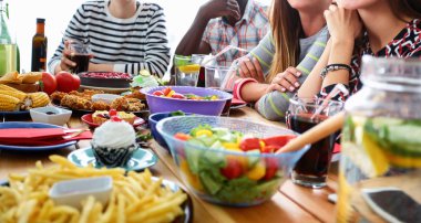 Bir grup insan ahşap masada otururken birlikte yemek yiyorlar.