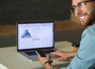 Genç adam kullanarak telefon ve dizüstü bilgisayarda çalışır.