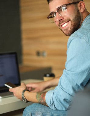 Genç adam kullanarak telefon ve dizüstü bilgisayarda çalışır.