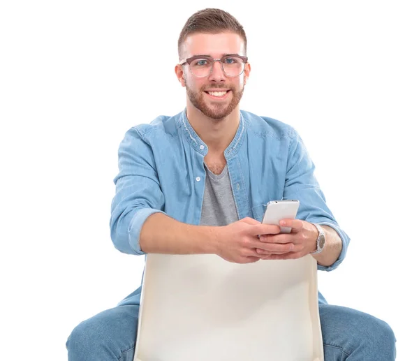 Sandalyede oturan ve cep telefonuyla genç adam — Stok fotoğraf