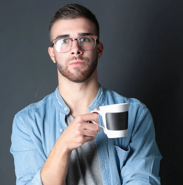 Portret van een knappe jongeman permanent en houden van een kopje koffie in zijn handen. — Stockfoto