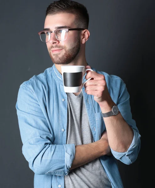 Portret van een knappe jongeman permanent en houden van een kopje koffie in zijn handen. — Stockfoto