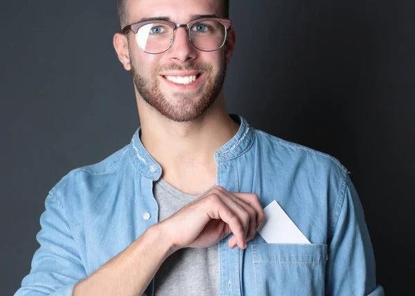 Young man holding a credit card standing on gray background. — Stock Photo, Image