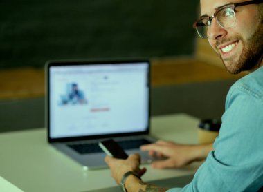 Genç adam kullanarak telefon ve dizüstü bilgisayarda çalışır.