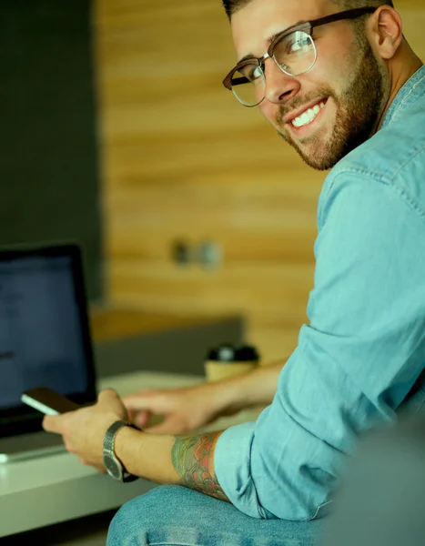 Молодой человек пользуется телефоном и работает на ноутбуке . — стоковое фото